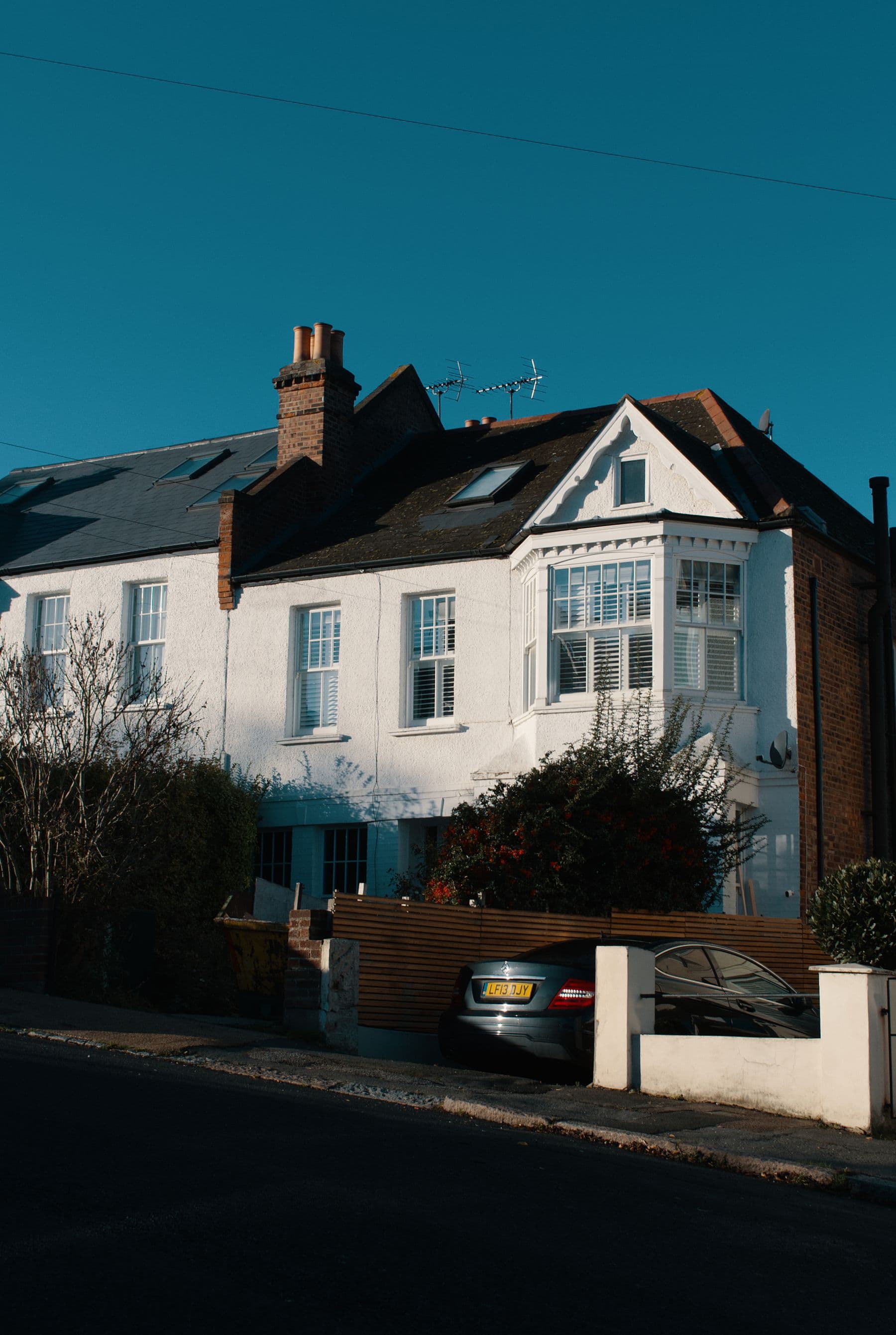 Sunlit UK terraced house with a slate roof and chimney stacks against a clear blue sky