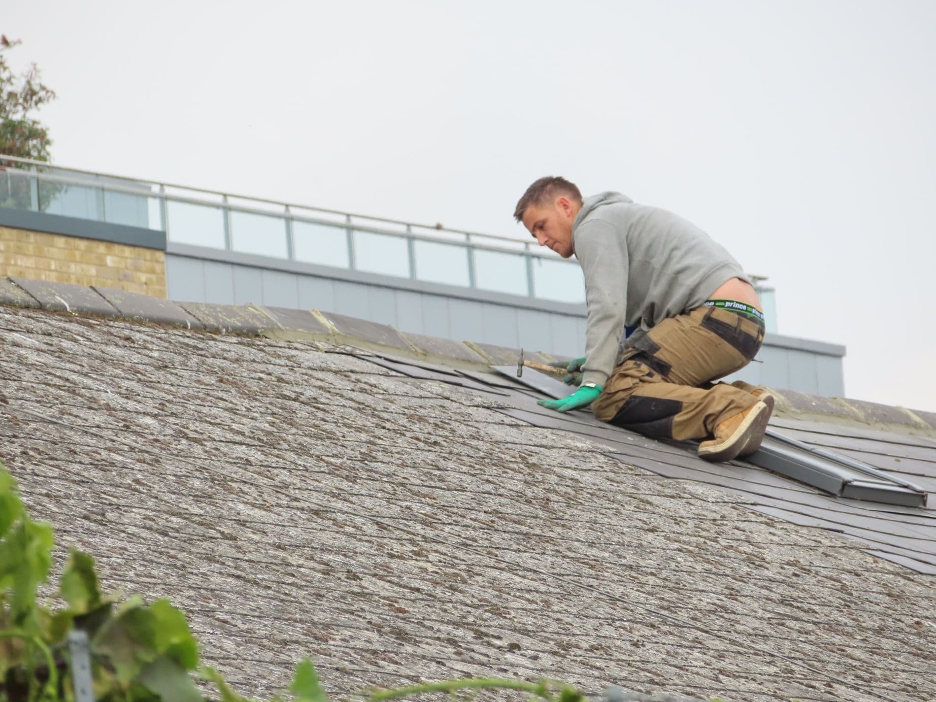 Roofer repairing tiles on a pitched roof in London
